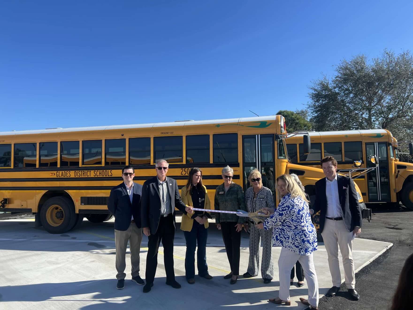 People cutting a ribbon in front of electric school buses
